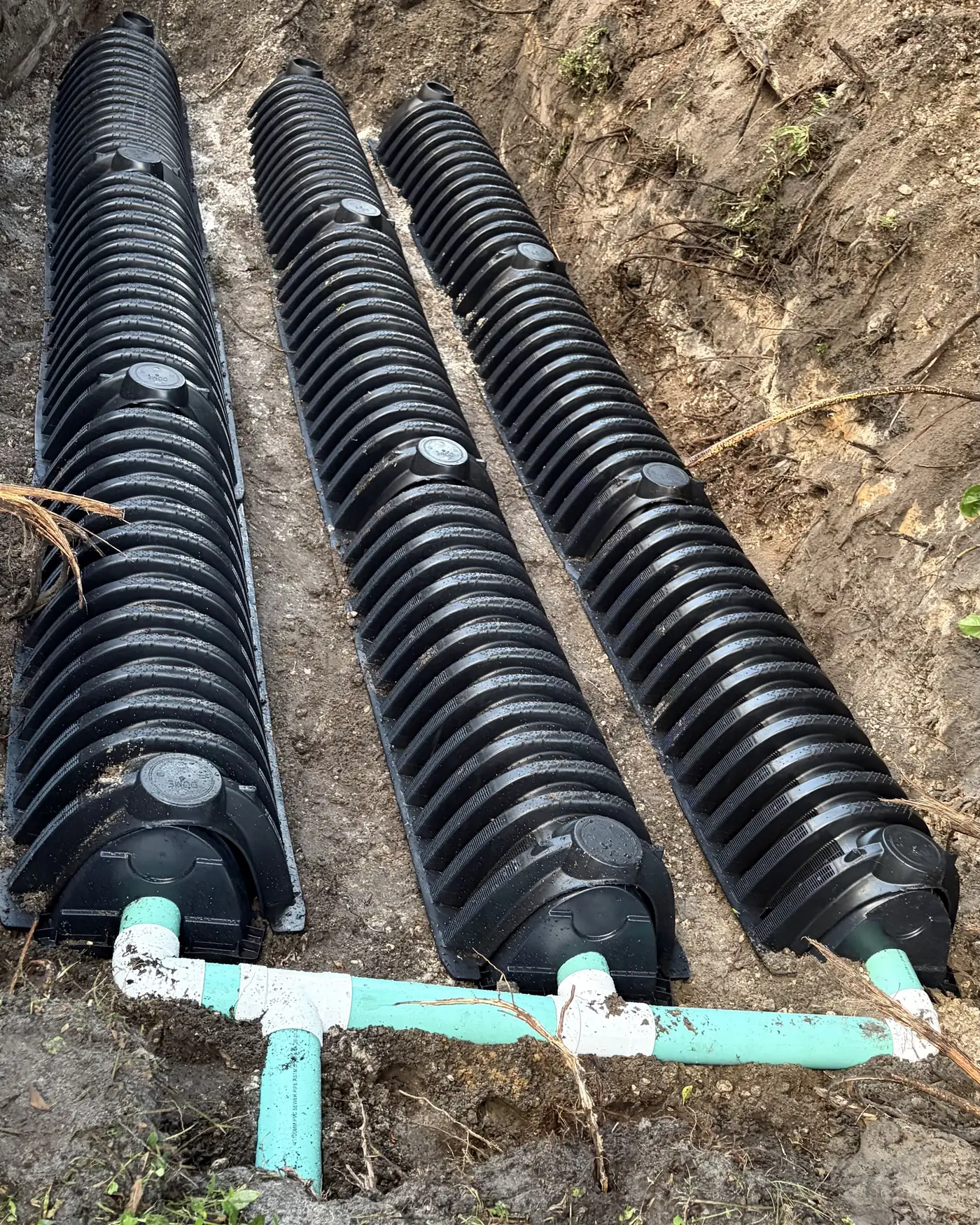 Three rows of drain field chambers joined by a pipe manifold in a freshly dug trench
