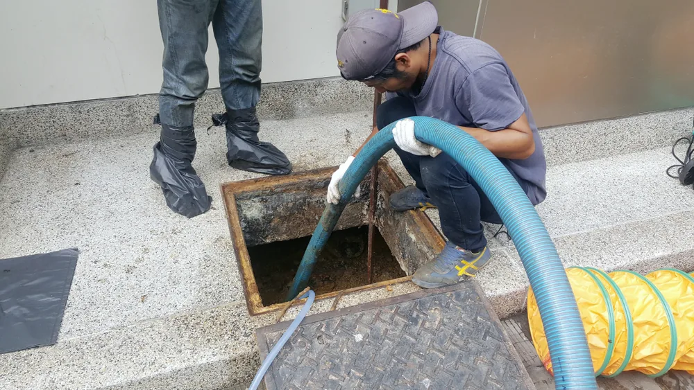 Crew member pumping out an indoor grease interceptor through an open floor hatch with a vacuum hose