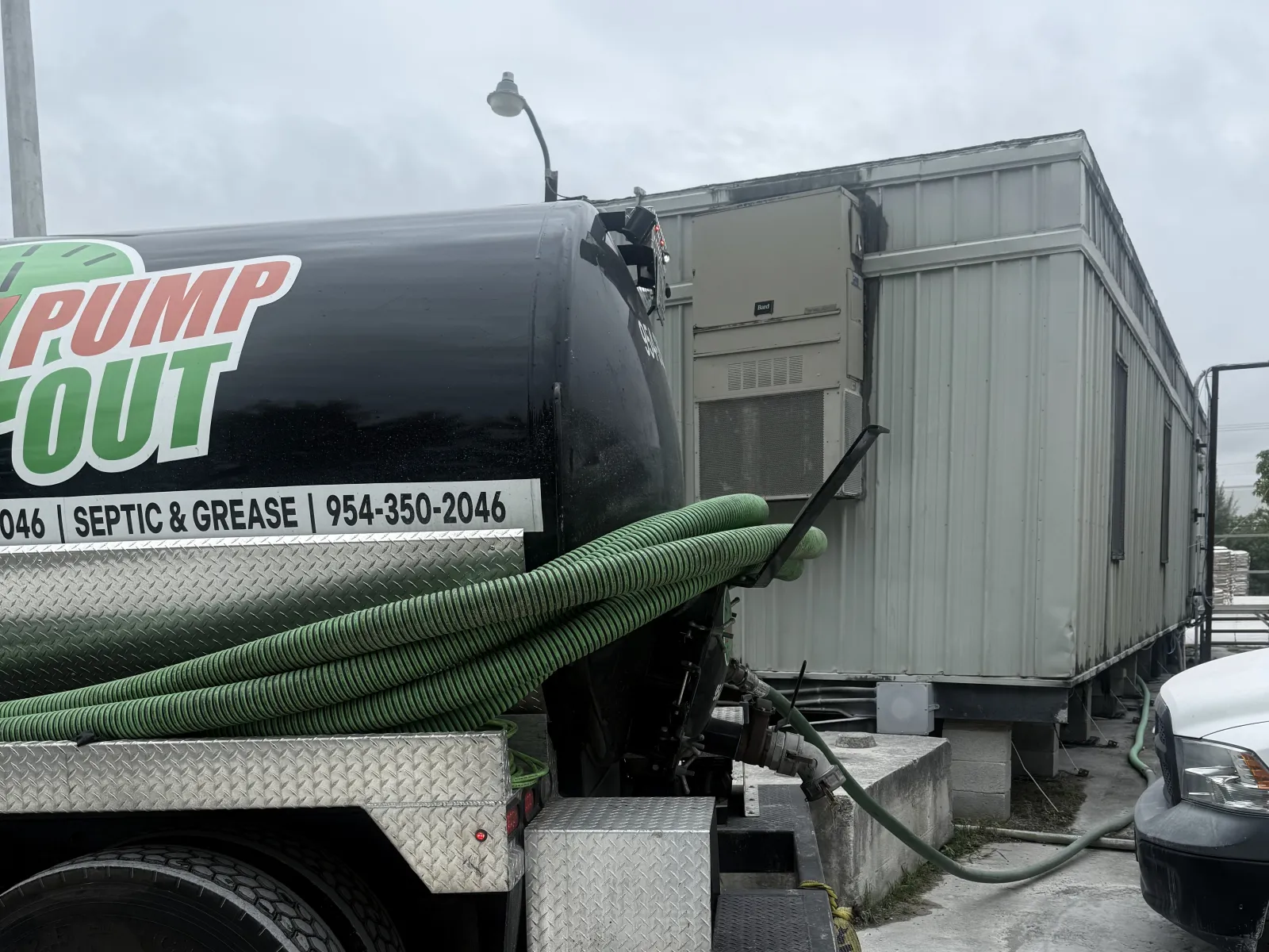 The 24-7 Pump Out vacuum truck parked beside a modular building with its green hose run out across the pavement