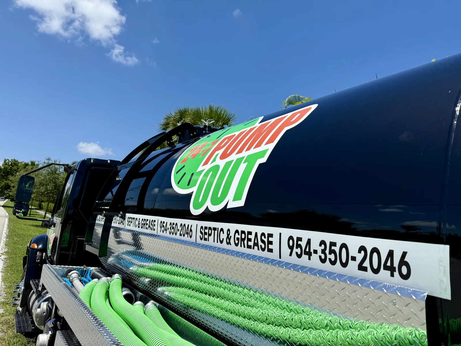 The 24-7 Pump Out vacuum truck with green suction hoses racked along the tank and the septic and grease decal on its side